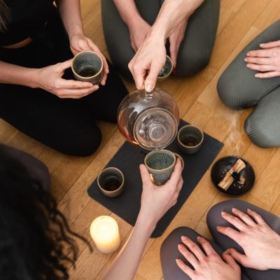 Young woman is pouring hot tea to her friends sitting around a tray during a tea ceremony.